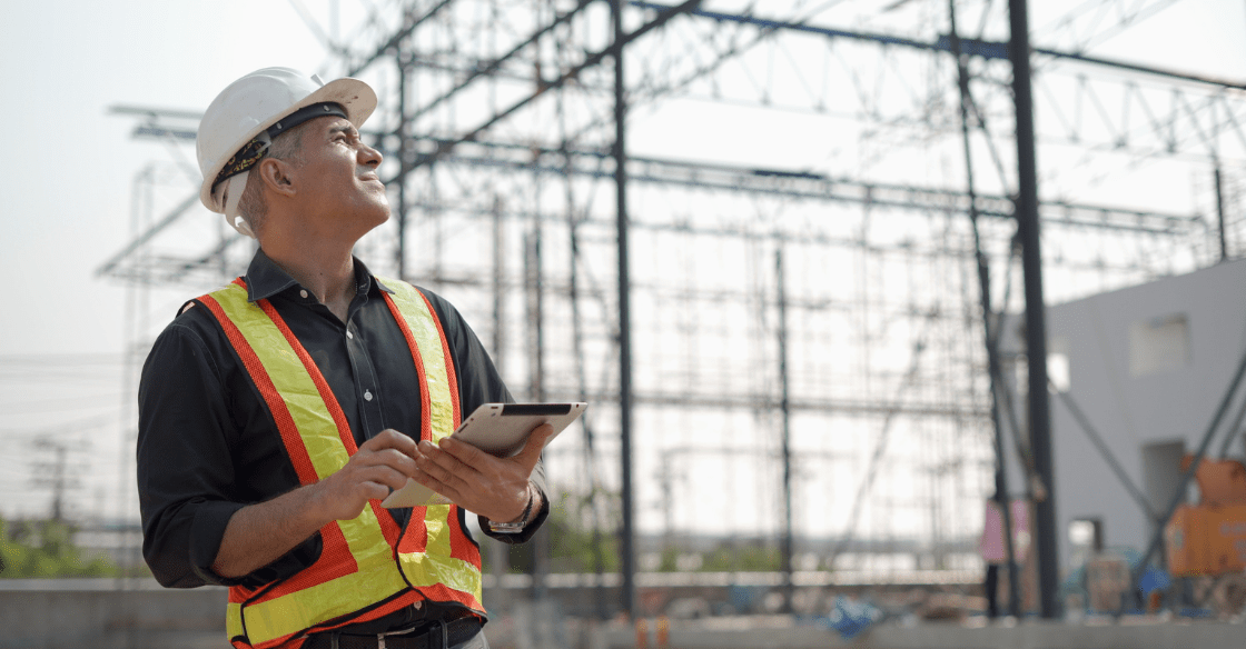 A construction worker squints in the heat while monitoring the weather on his tablet.