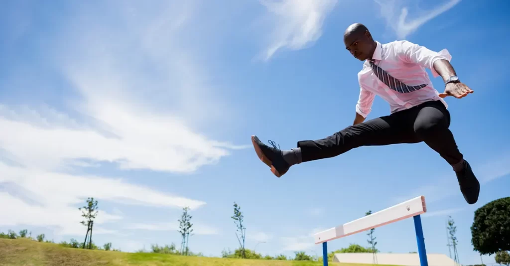 Businessman jumping over a track hurdle